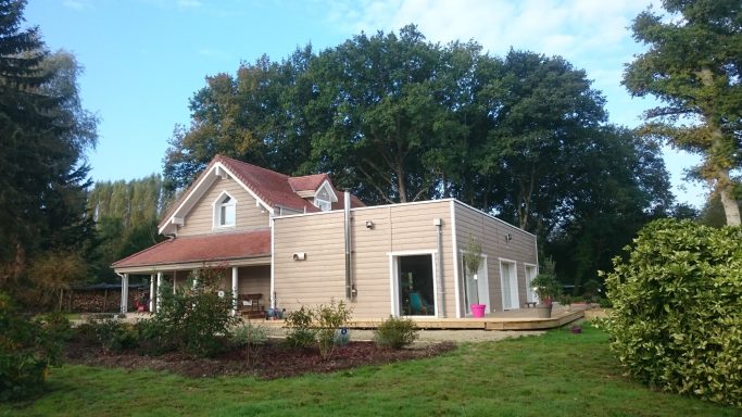 Maison en bordure d'un jardin verdoyant, avec un toit rouge et une façade claire.