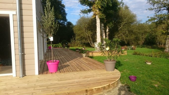 Terrasse en bois avec des pots de fleurs, entourée d'un jardin verdoyant.