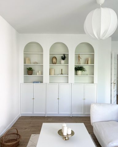 Étagère blanche avec niches arrondies, décorée d'objets et plantes, canapé blanc.
