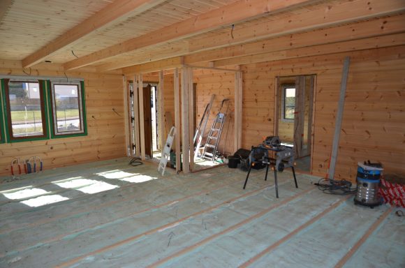 Intérieur d'une maison en cours de construction, murs en bois et outils présents.